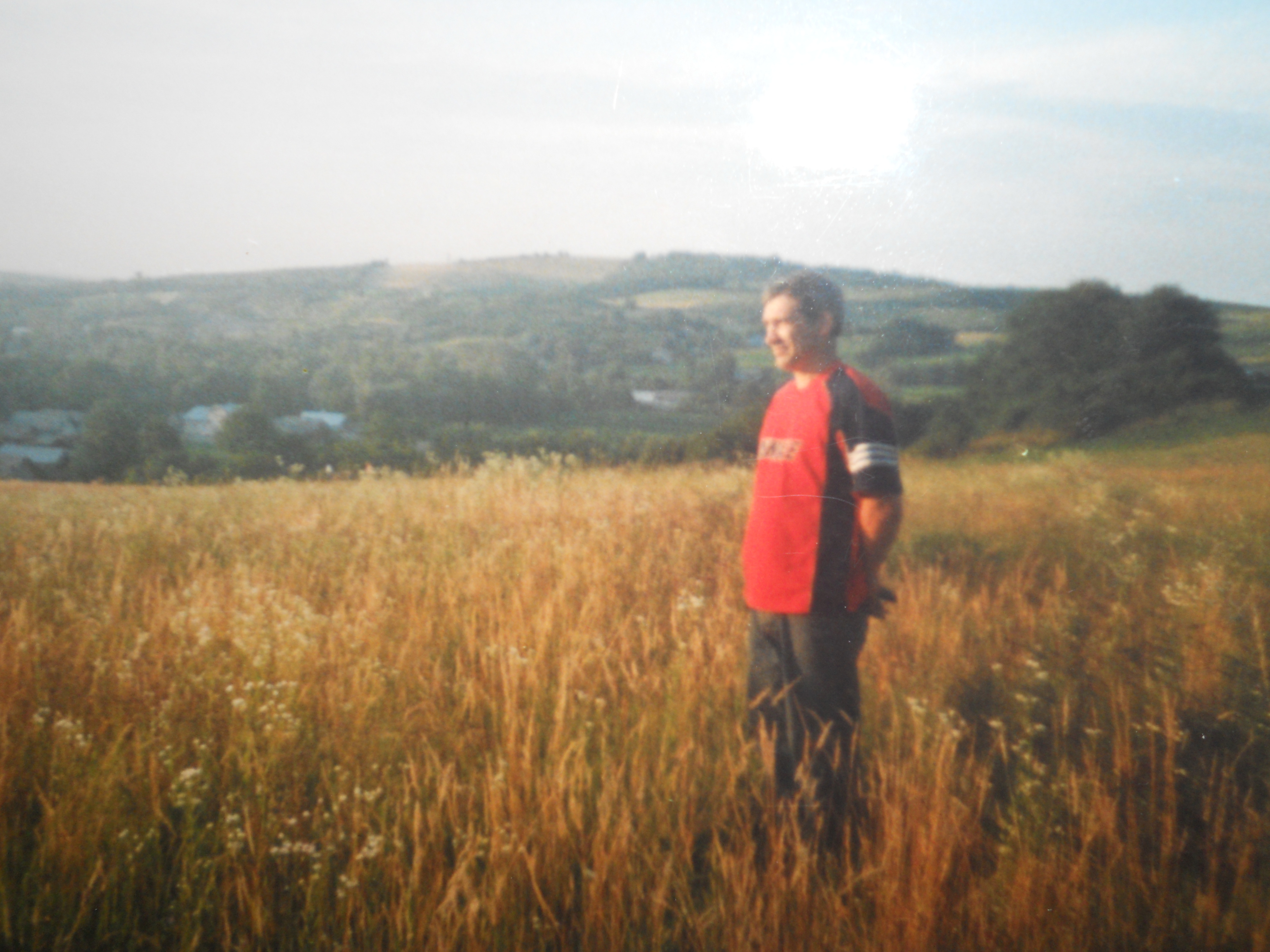 Rostyslav, Ukrainian landscape painter, standing in a warm golden field at the edge of a village, soft rolling hills behind — the kind of light that becomes his paintings.